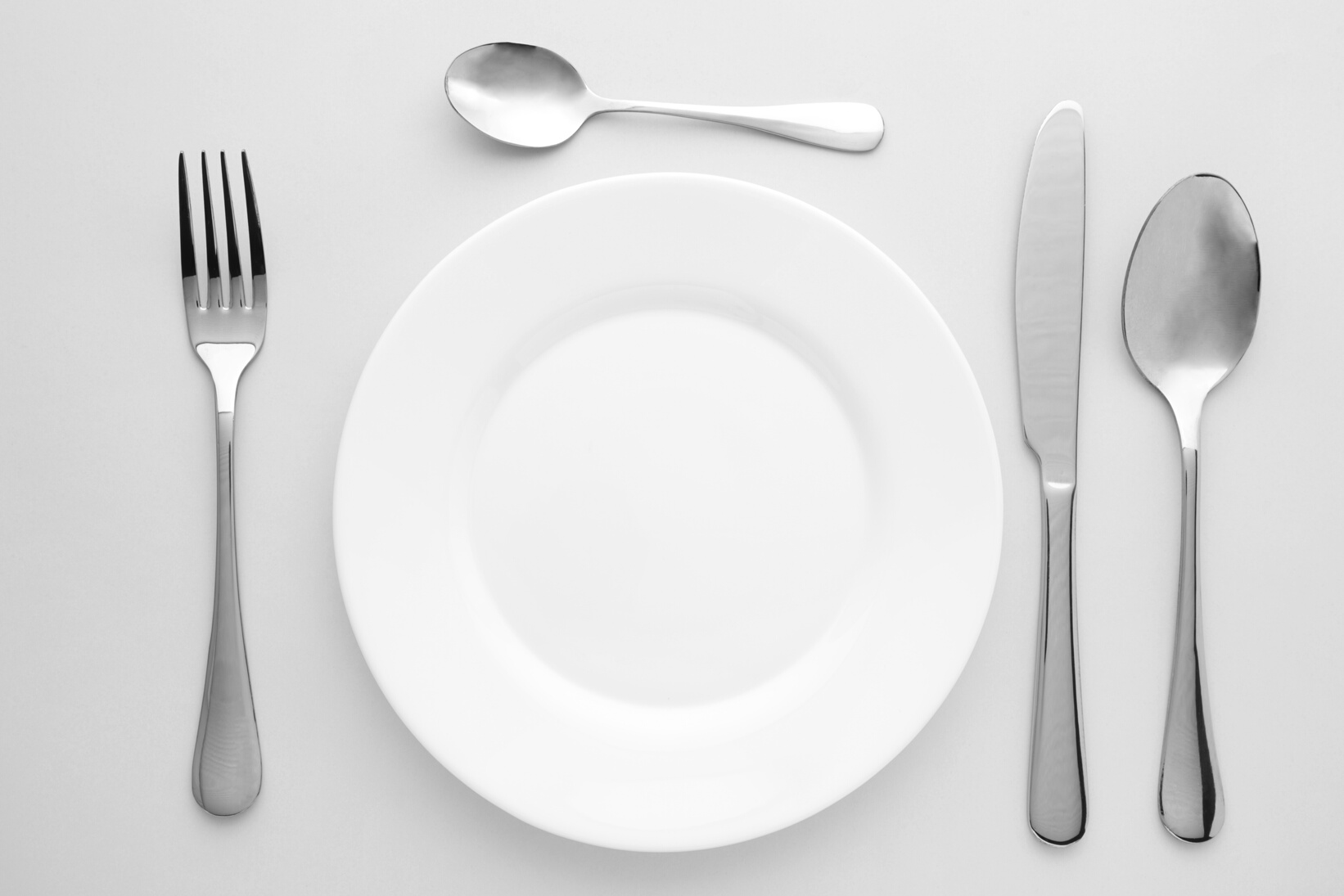 Table Setting with White Plates, and Cutlery - Fork, Spoon and Knife. Shot from above. Copy Space on Empty Plate.